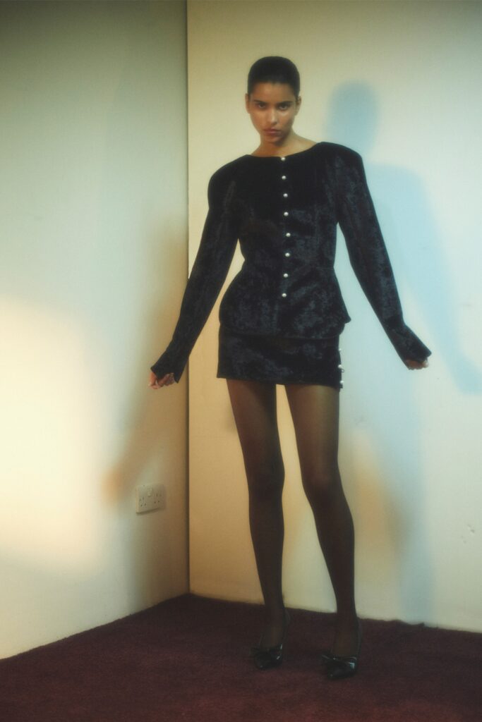 A fitted black velvet dress with long sleeves, a collared neckline, and button details.