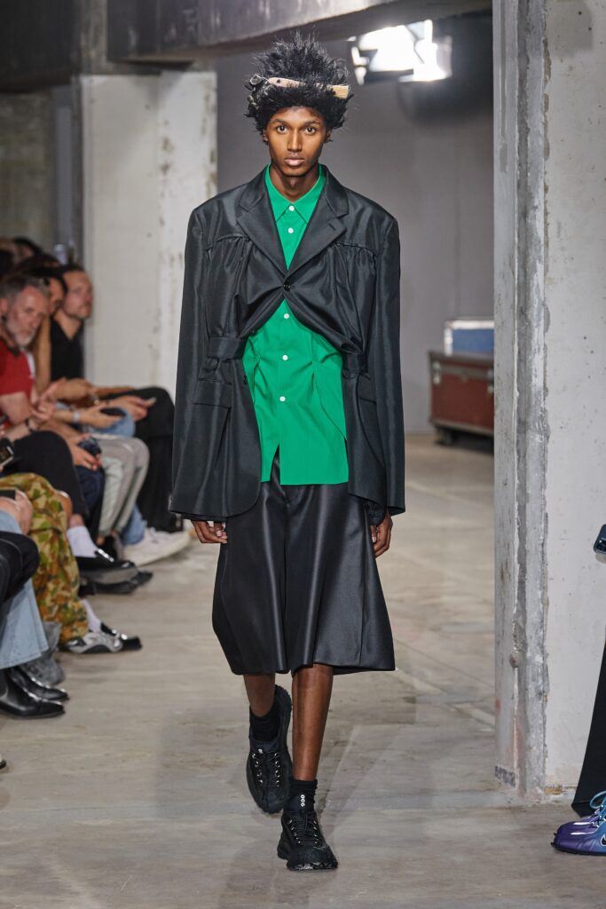 A relaxed black jacket layered over a green collared shirt and a black skirt.