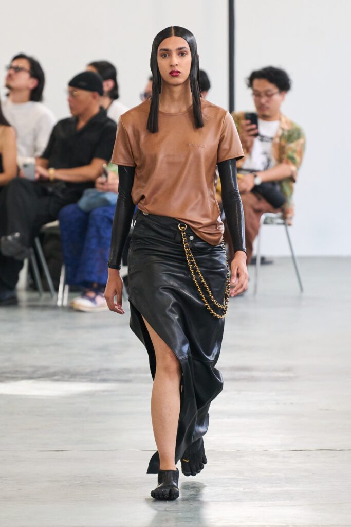 A fitted brown leather top paired with a high-waisted black leather skirt featuring an asymmetric slit.