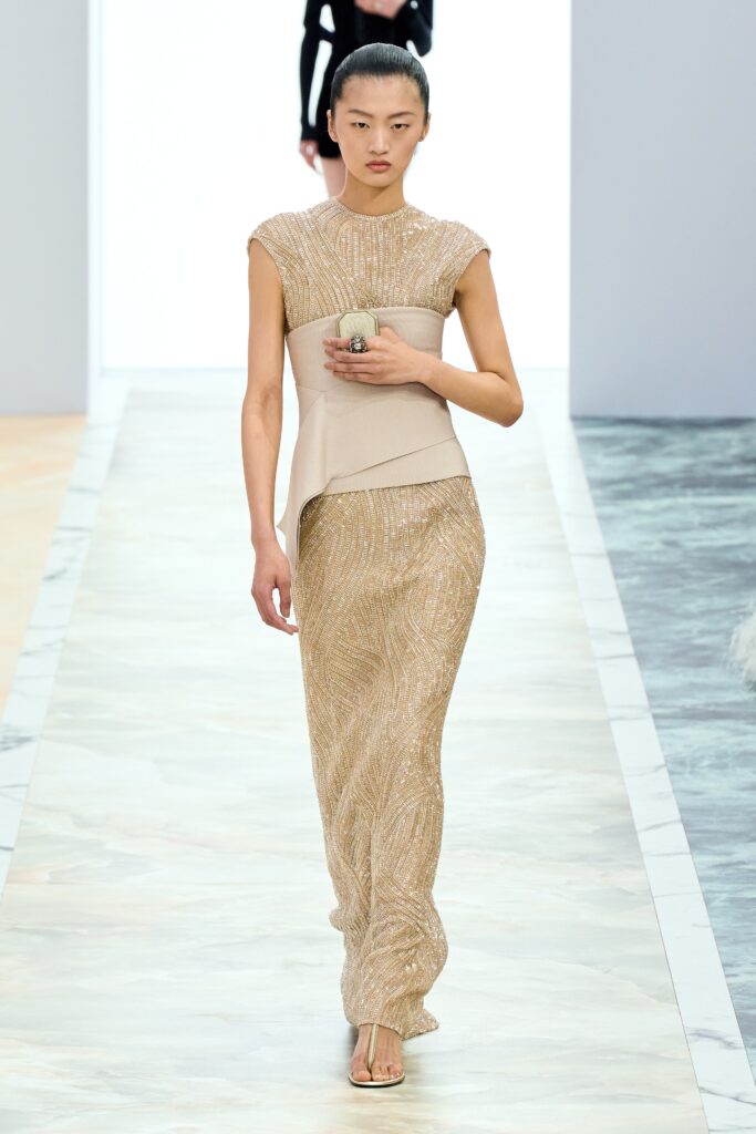 A fitted beige silk dress with a sleeveless design and high-neck construction.