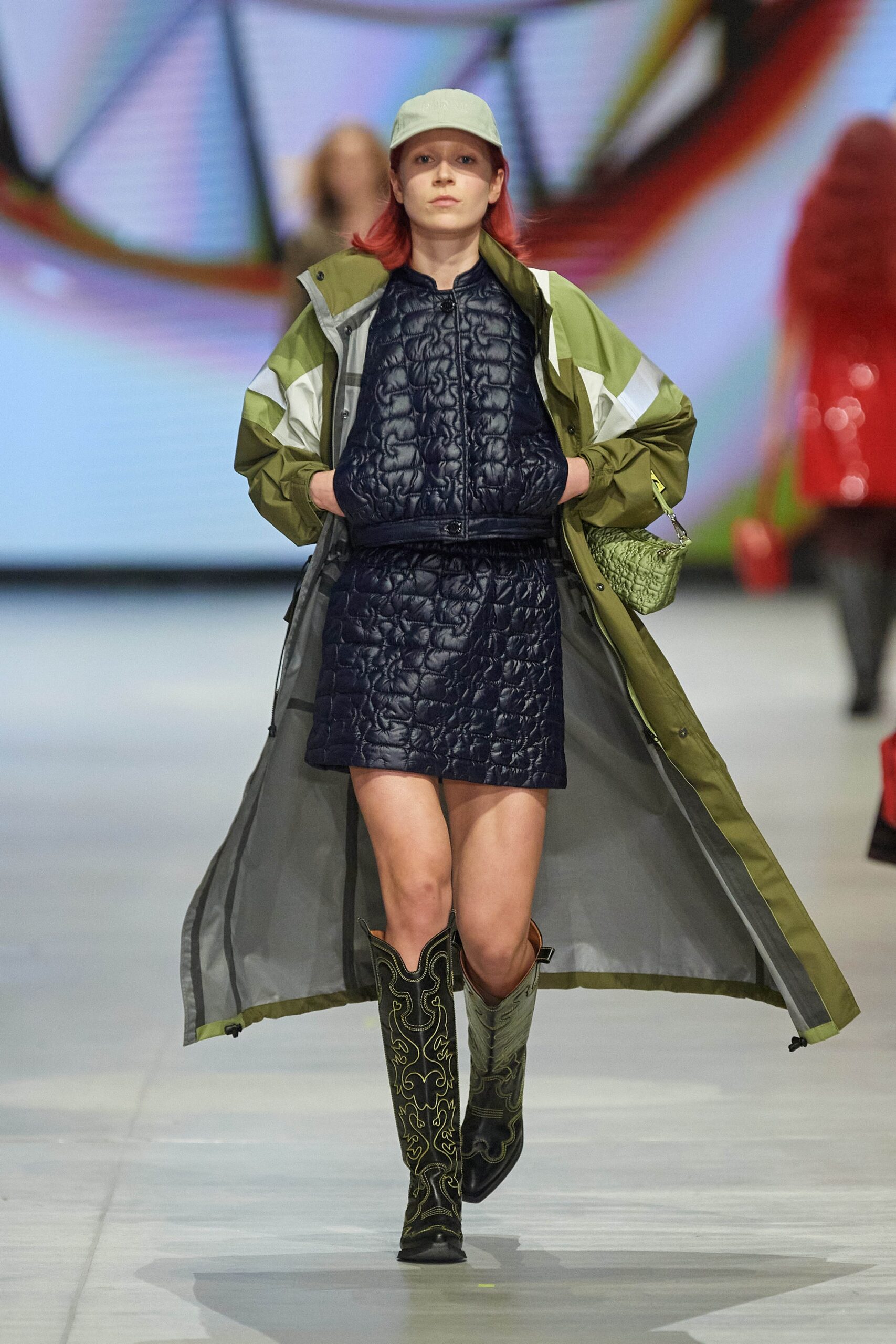 A fitted green coat layered over a sleeveless navy dress with an asymmetric design.