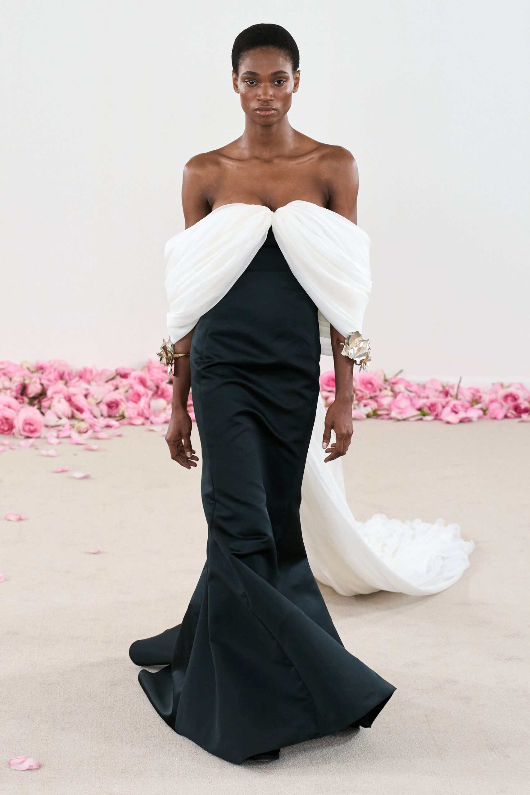 A fitted black silk strapless gown with a V-neckline and flared silhouette, complemented by white draped sleeves.