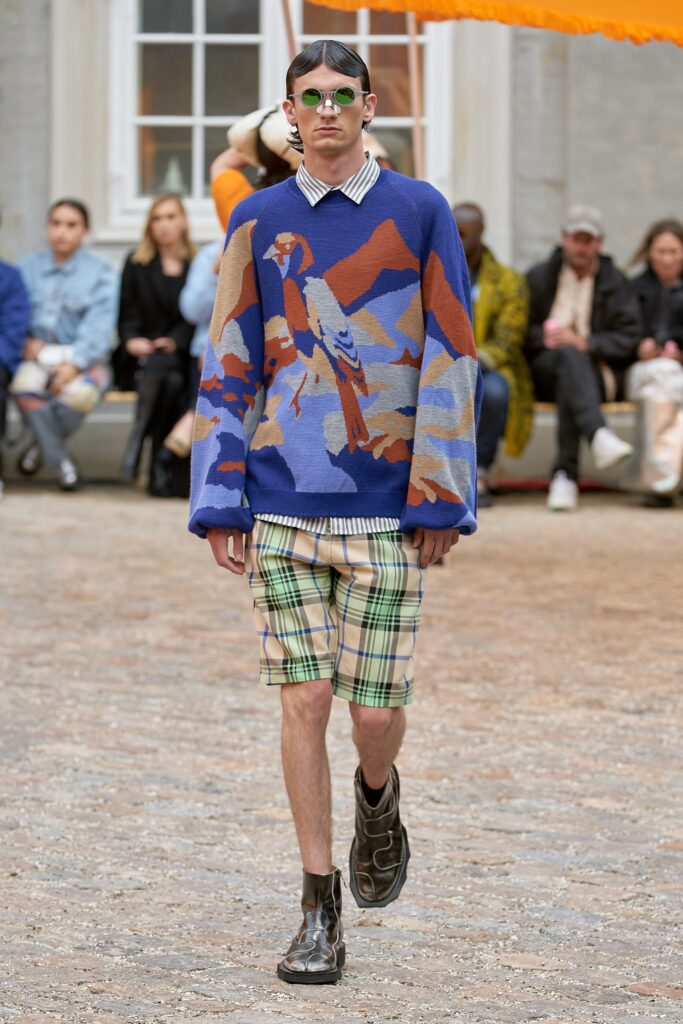 An oversized multicolor sweater with long sleeves paired with plaid shorts.