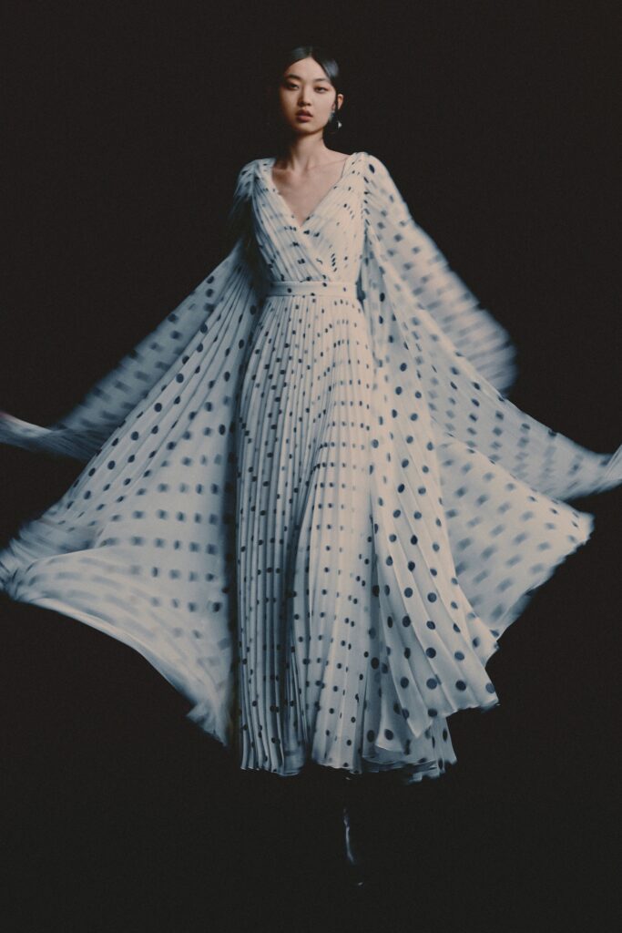 A fitted white silk dress with long sleeves, a V-neckline, and pleated polka-dot design.