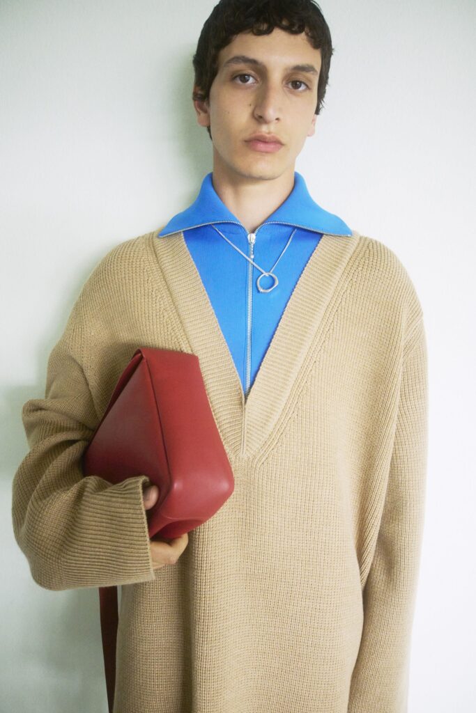 An oversized beige v-neck sweater layered over a blue shirt, paired with a stylish bag.