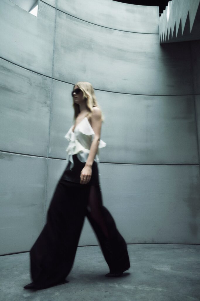 A relaxed white ruffled sleeveless top paired with black wide-leg pants.
