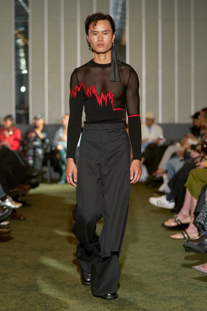 A relaxed black mesh top with red accents and high-neck paired with relaxed black pants.