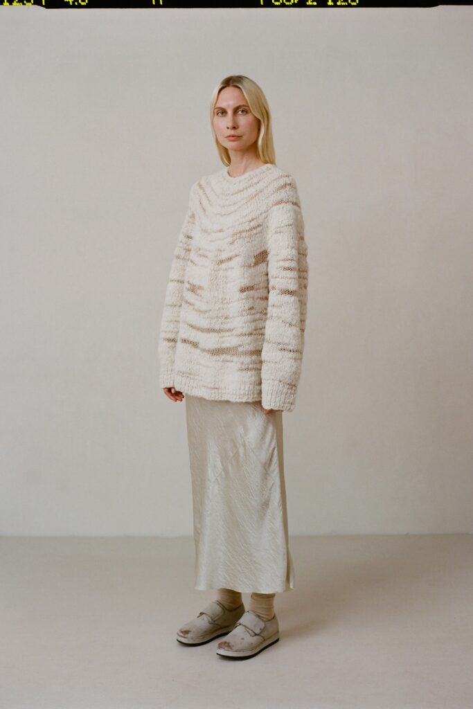 An oversized white wool sweater paired with a cream silk skirt, creating a layered look.