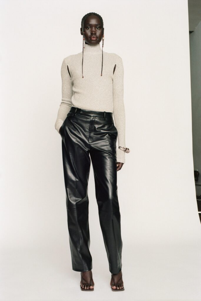 A fitted beige knit long-sleeve top paired with black leather straight-leg pants.