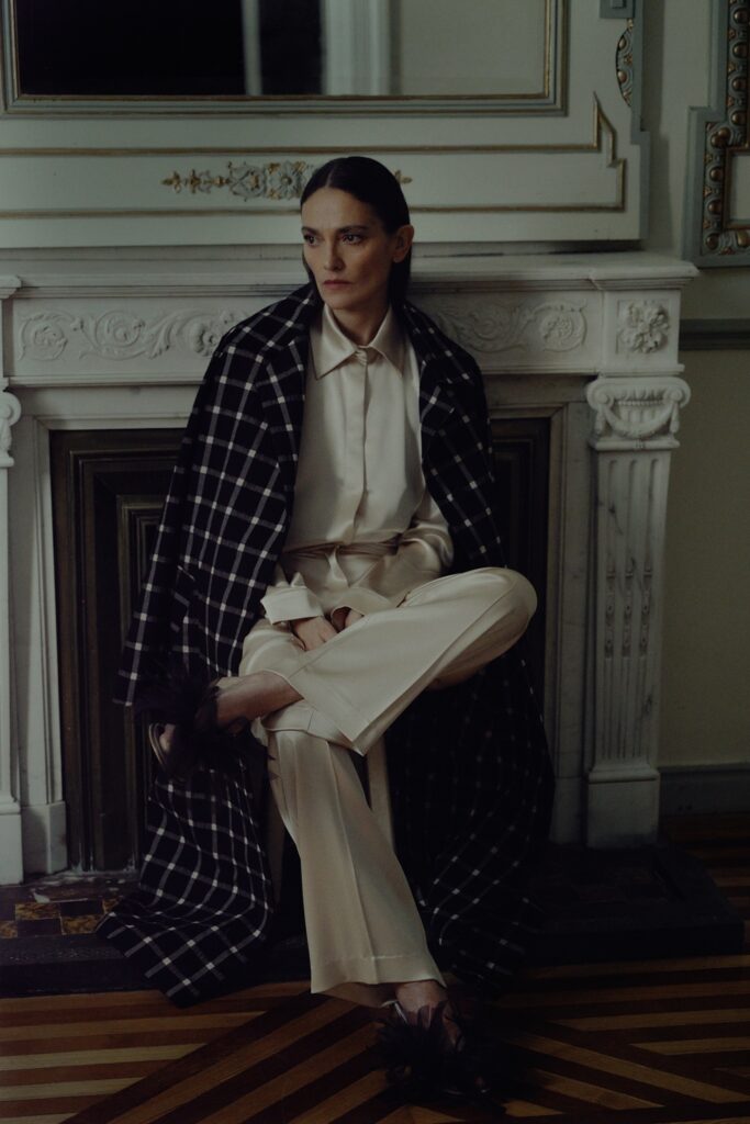 A relaxed black checked coat paired with a long-sleeve collared white shirt.