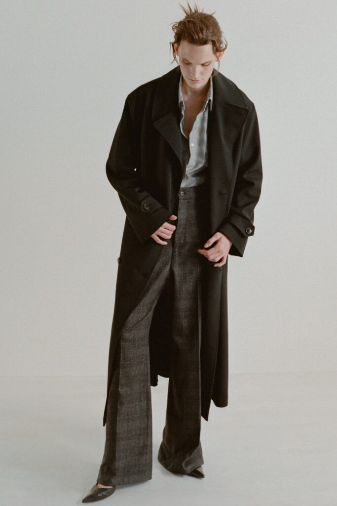 A relaxed black wool coat paired with wide-leg gray pants and a collared shirt.
