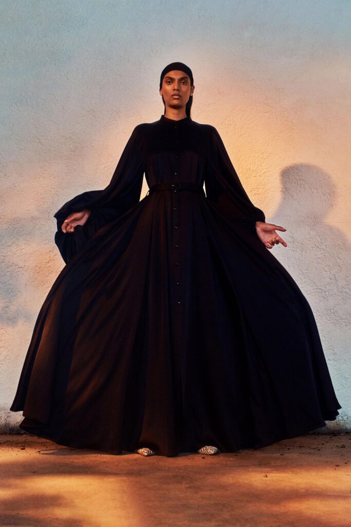 A fitted black silk long-sleeve dress with a tiered design and collared neckline.