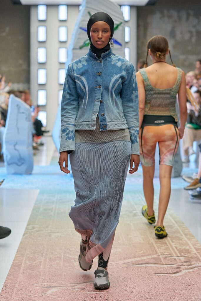 A fitted blue denim jacket with long sleeves paired with a layered denim skirt.
