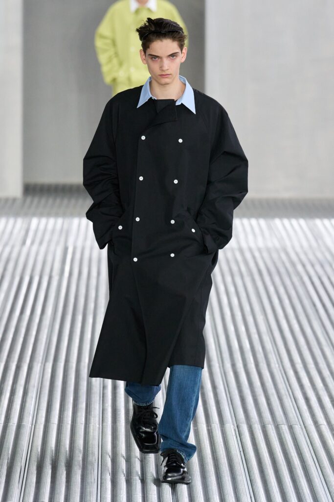 A relaxed black coat with a collared neckline, paired with blue pants and button details.