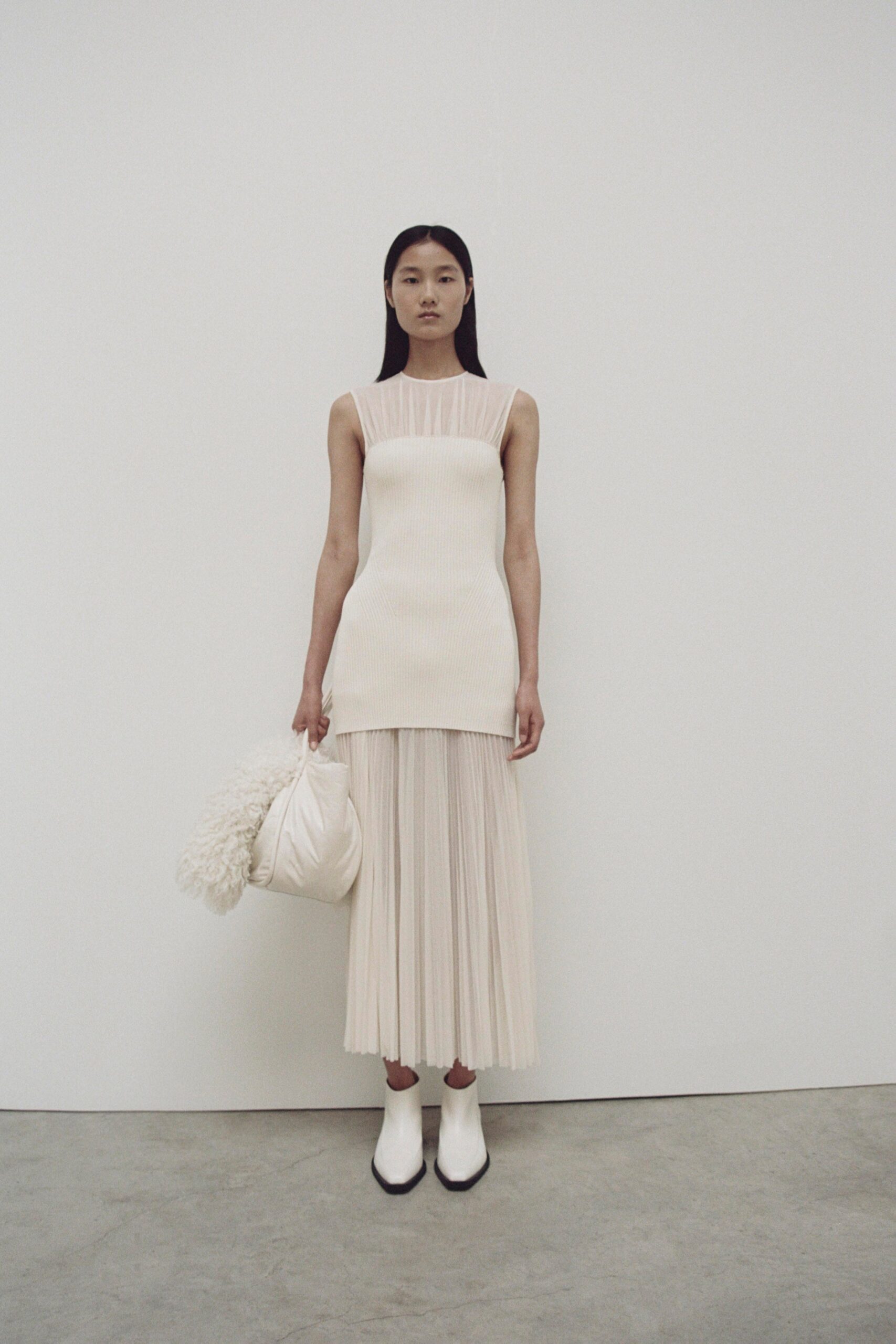 A fitted white sleeveless dress with a high neckline and pleated design.