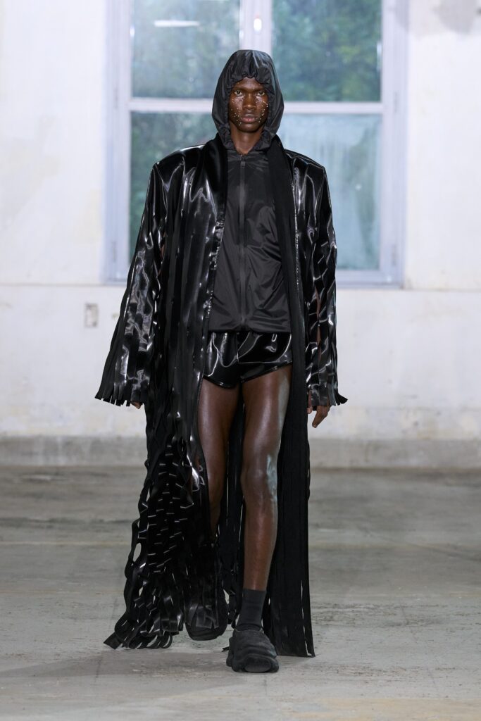A relaxed black leather coat with a hood and fringed details, paired with black shorts.