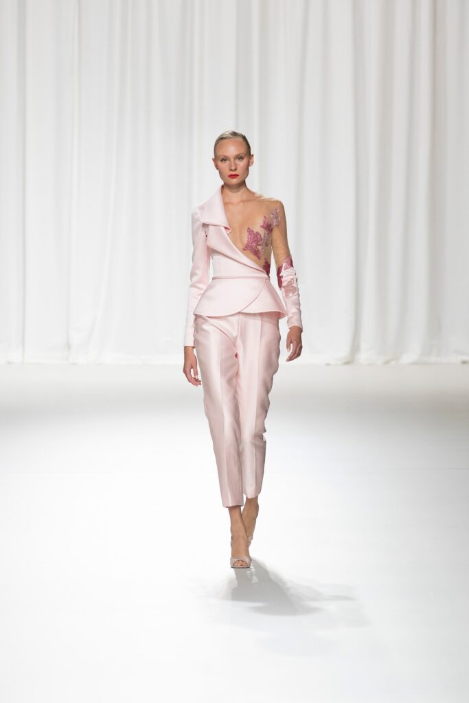 A fitted pink silk jacket with a V-neckline and asymmetric design paired with matching pants.