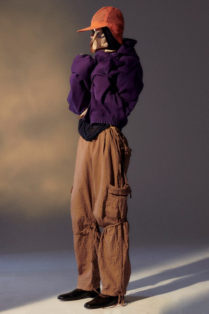 A relaxed purple jacket with long sleeves paired with brown pants featuring a zippered detail.
