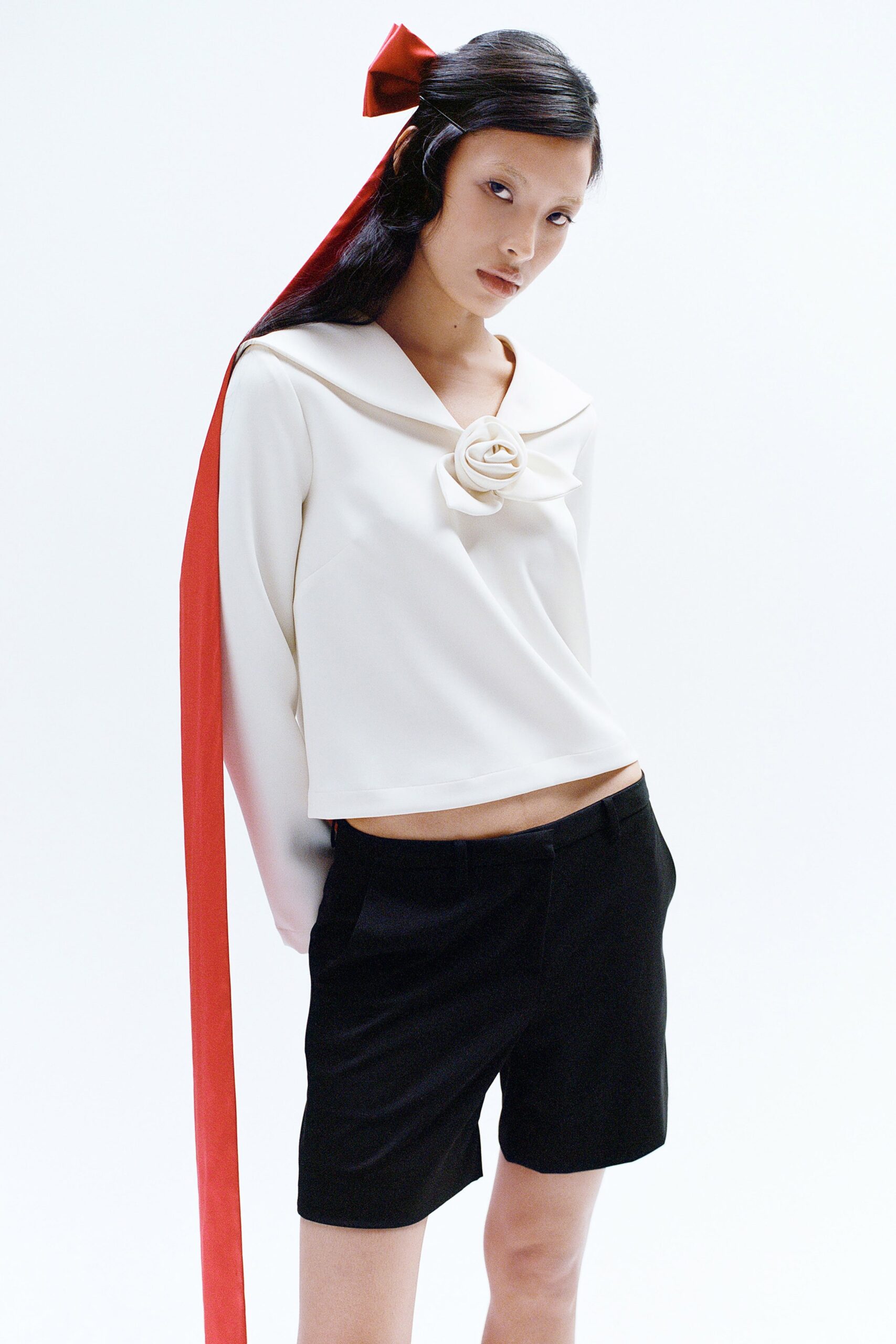 A fitted white long-sleeve top with a collar paired with black shorts and a red ribbon detail.