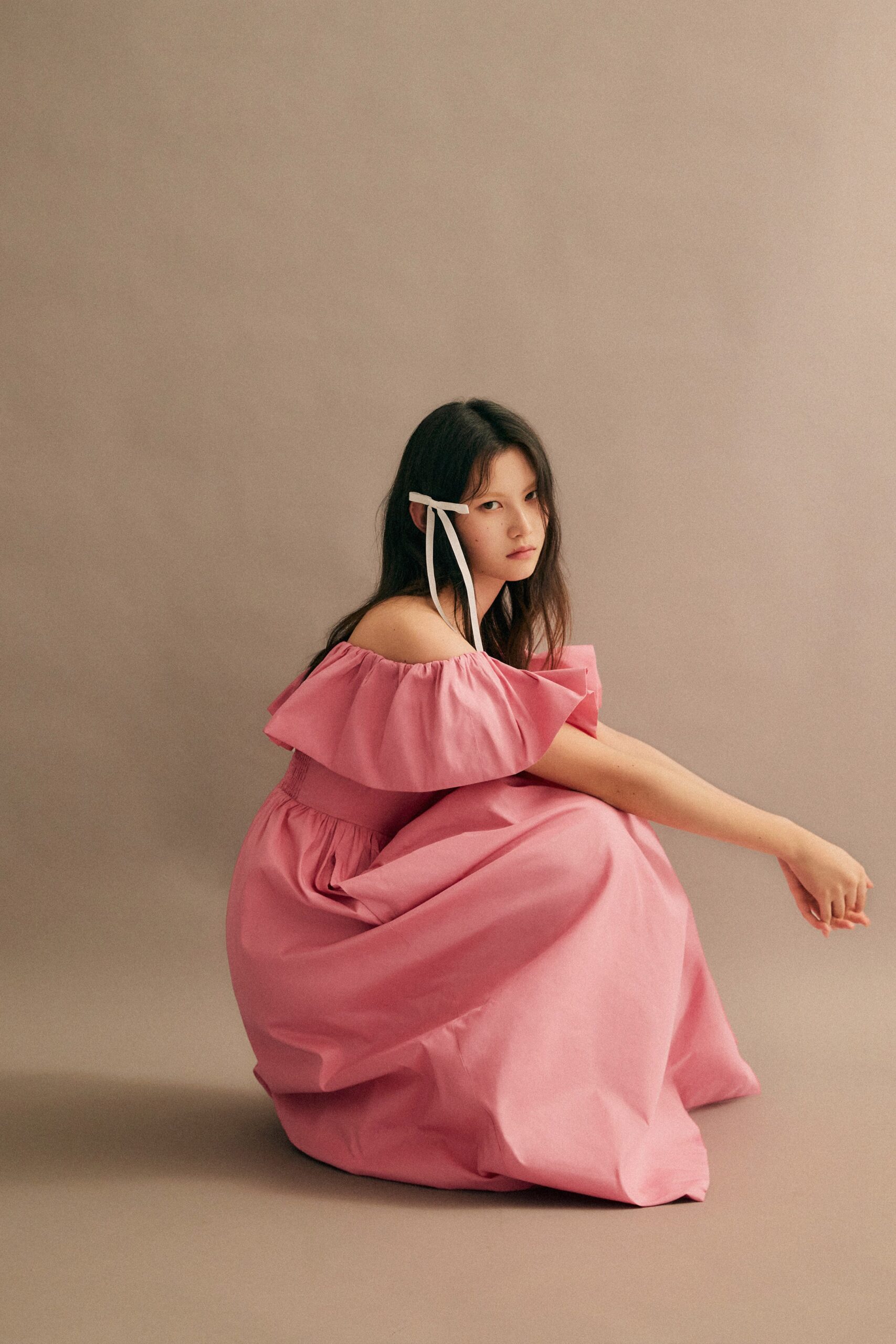 A relaxed pink cotton off-shoulder dress with ruffled details and a tiered silhouette.