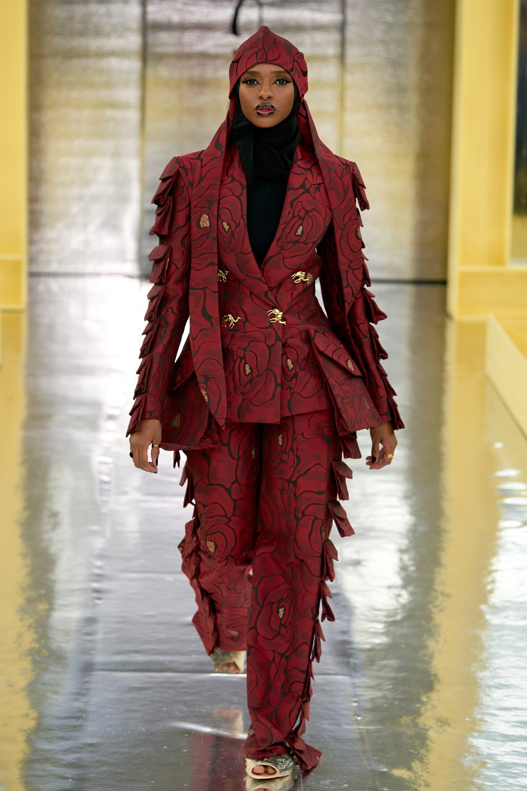 A fitted red silk suit with long sleeves, a collared design, and layered embroidered details.