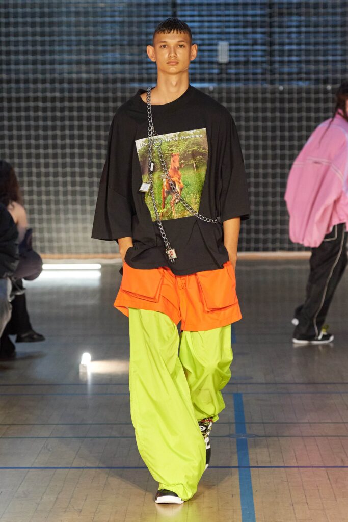 A relaxed black shirt paired with layered orange and green pants for a bold street style look.