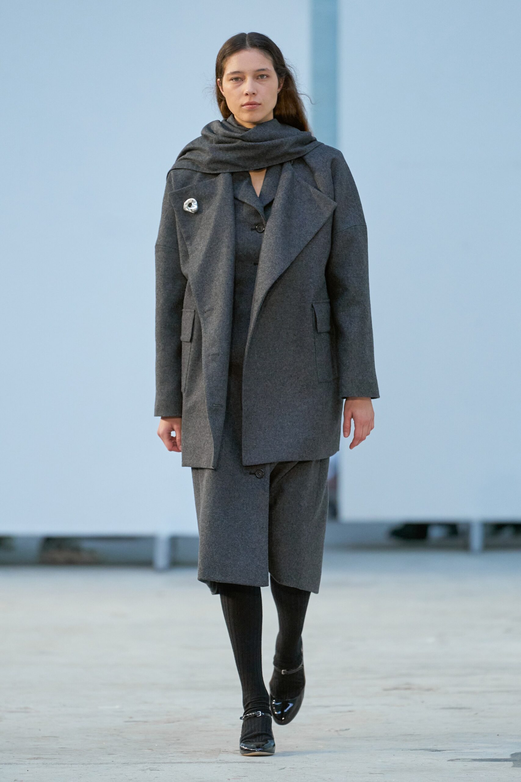 A relaxed gray wool coat with long sleeves and collared design, paired with wide-leg pants.