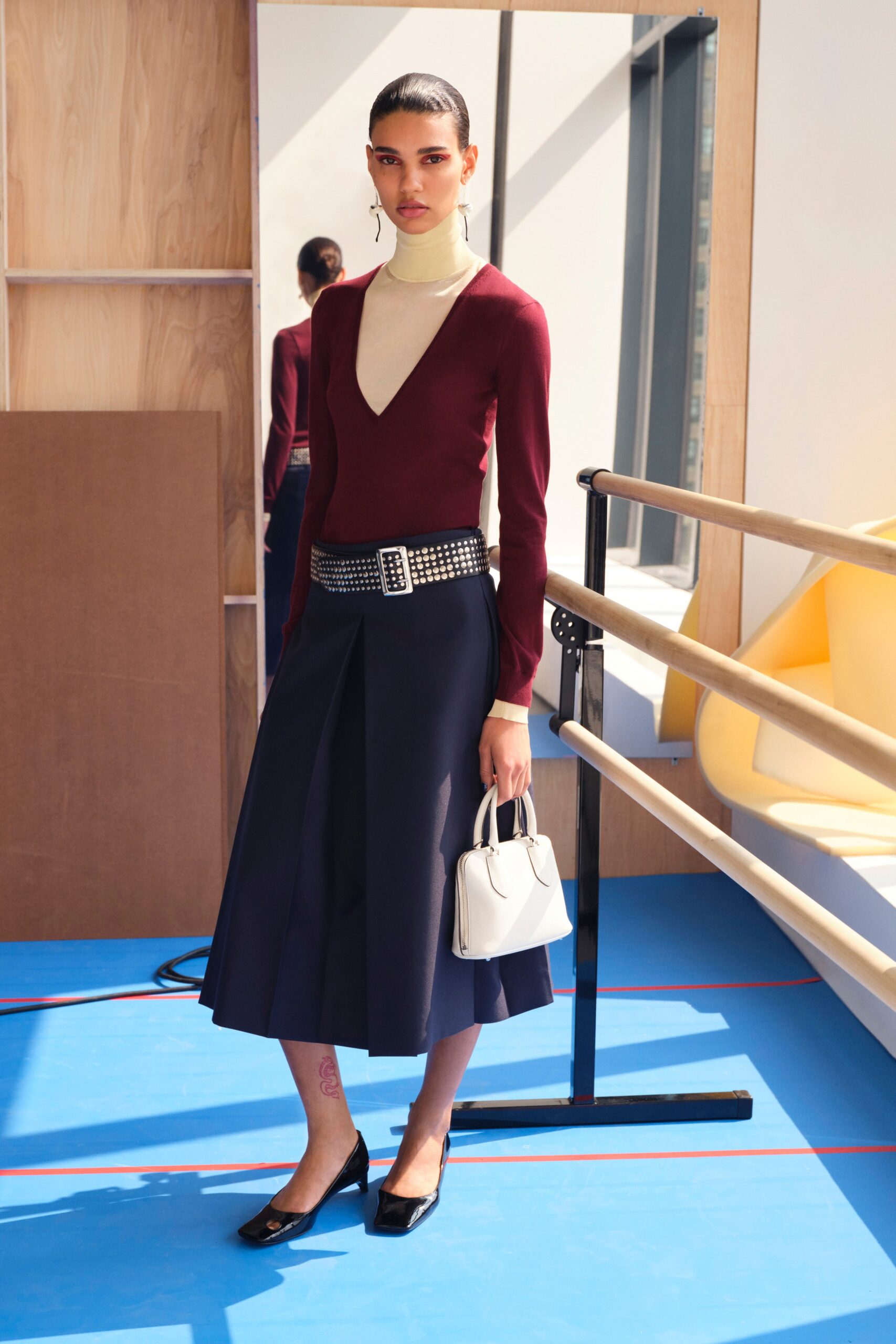 A fitted burgundy long-sleeve top with a V-neck paired with a pleated navy skirt.