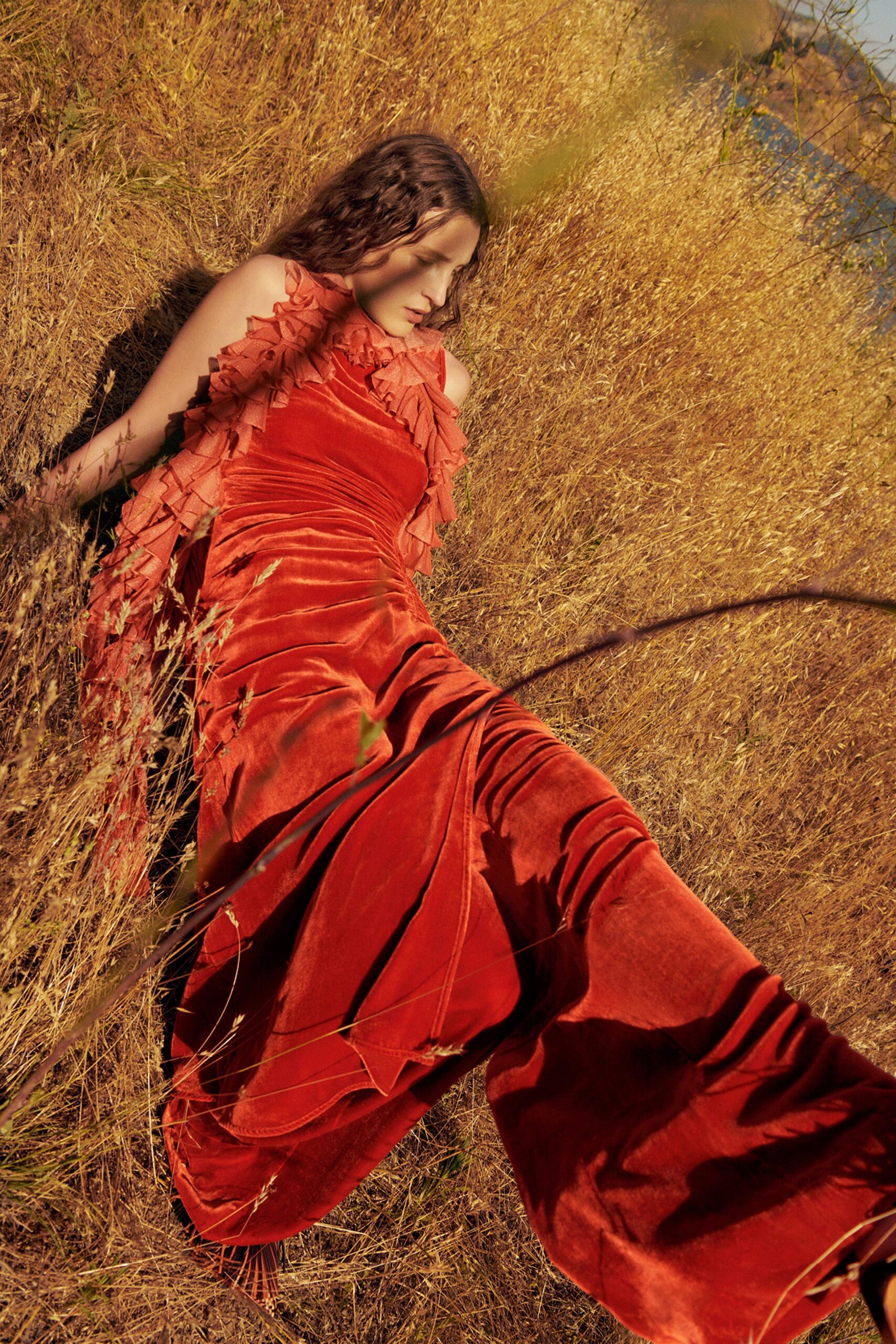 A fitted red velvet dress with a high neckline and ruffled details, cascading to a maxi length.