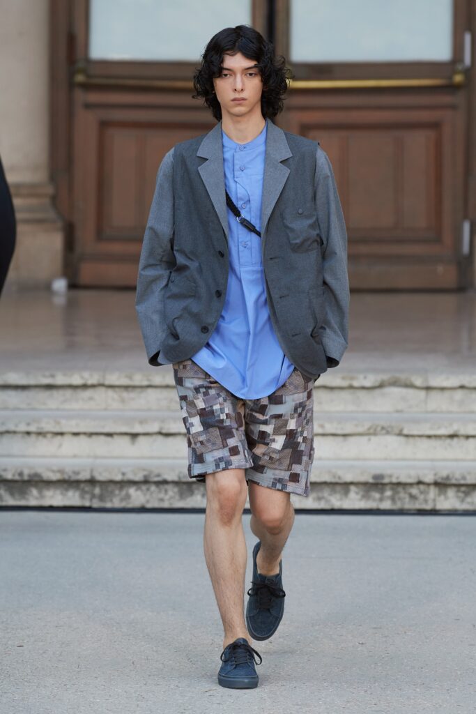 A relaxed gray jacket over a blue collared shirt paired with printed shorts.
