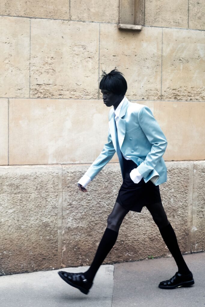A fitted blue jacket with a collared neckline paired with black shorts, featuring an asymmetric design.