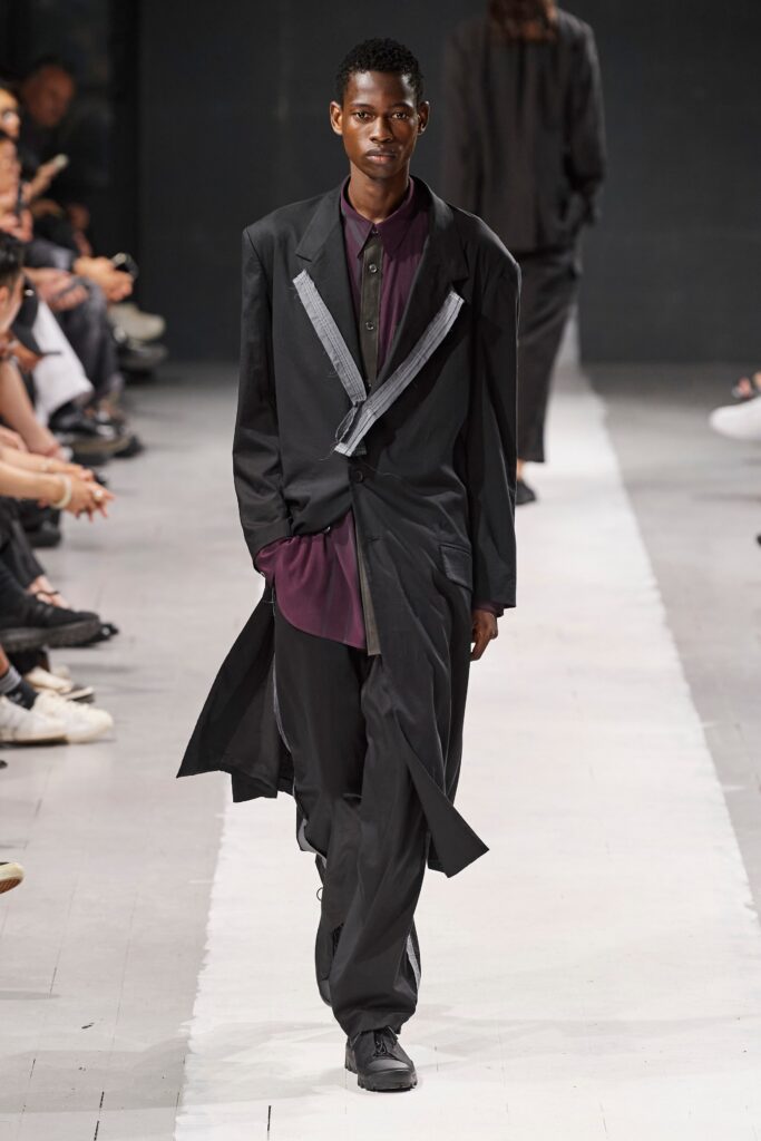 A relaxed black jacket with long sleeves and a collared neckline, paired with matching pants featuring an asymmetric design.
