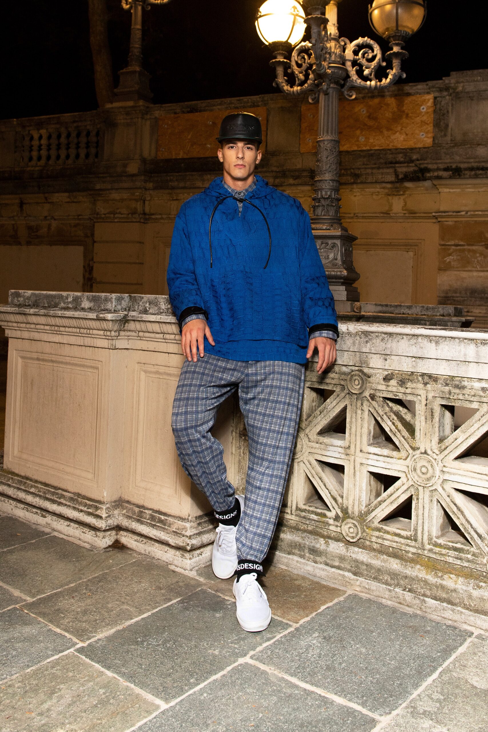 A relaxed blue hoodie with a hood paired with checked gray pants.