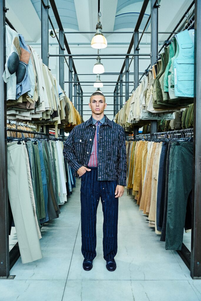 A fitted blue denim jacket with long sleeves and collared design paired with striped pants.