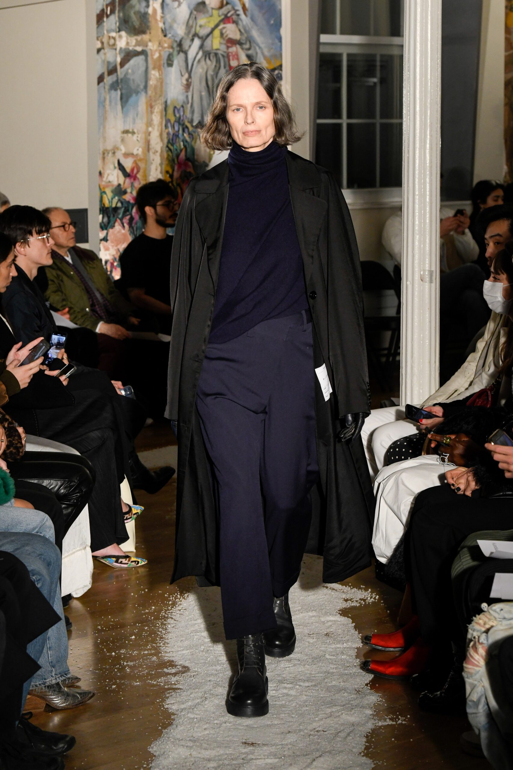 A relaxed black wool coat paired with navy pants, featuring a long-sleeve and collared design.