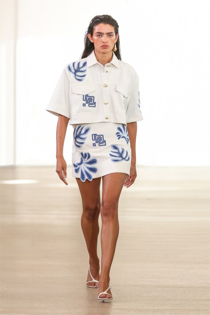 A fitted white cotton top with short sleeves and a collared design, paired with a mini embroidered skirt.