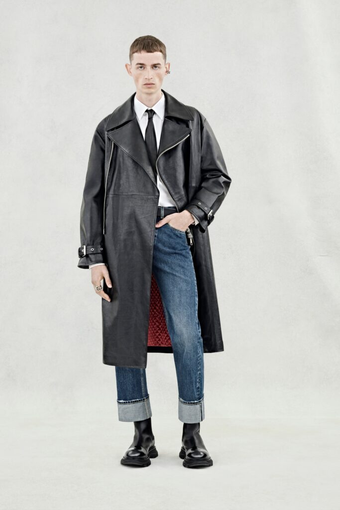 A fitted black leather coat with a collared neckline paired with fitted blue denim pants.