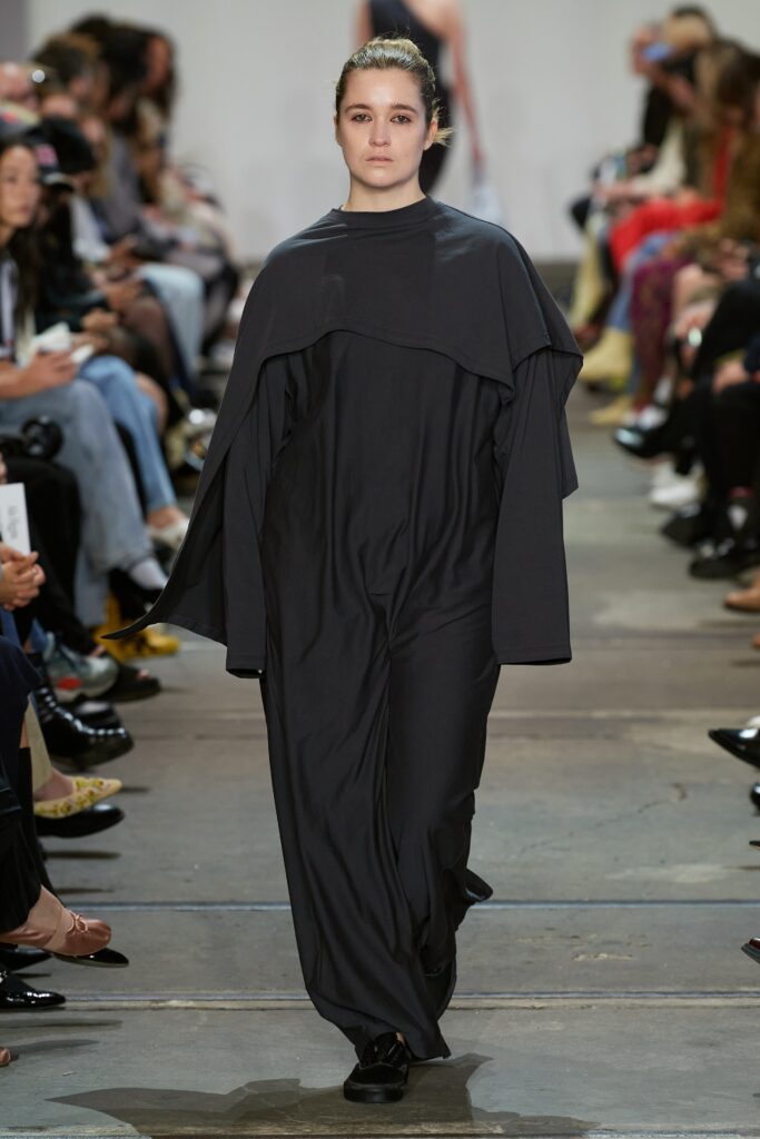 A relaxed black long-sleeve dress with a high neckline and asymmetric design.