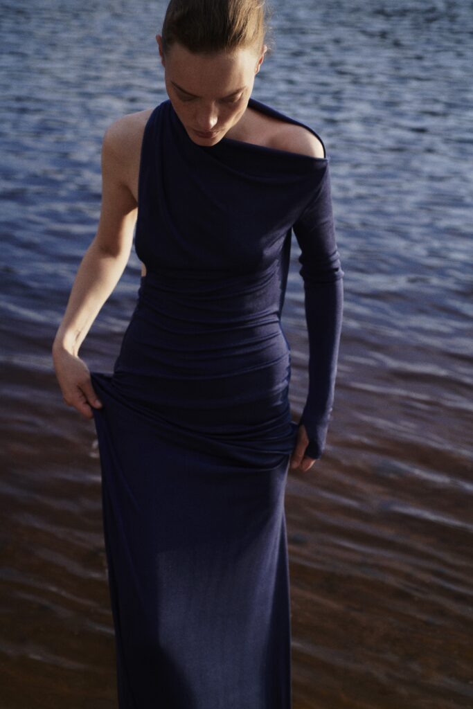 A fitted blue silk dress with an asymmetric design and high-neck construction.