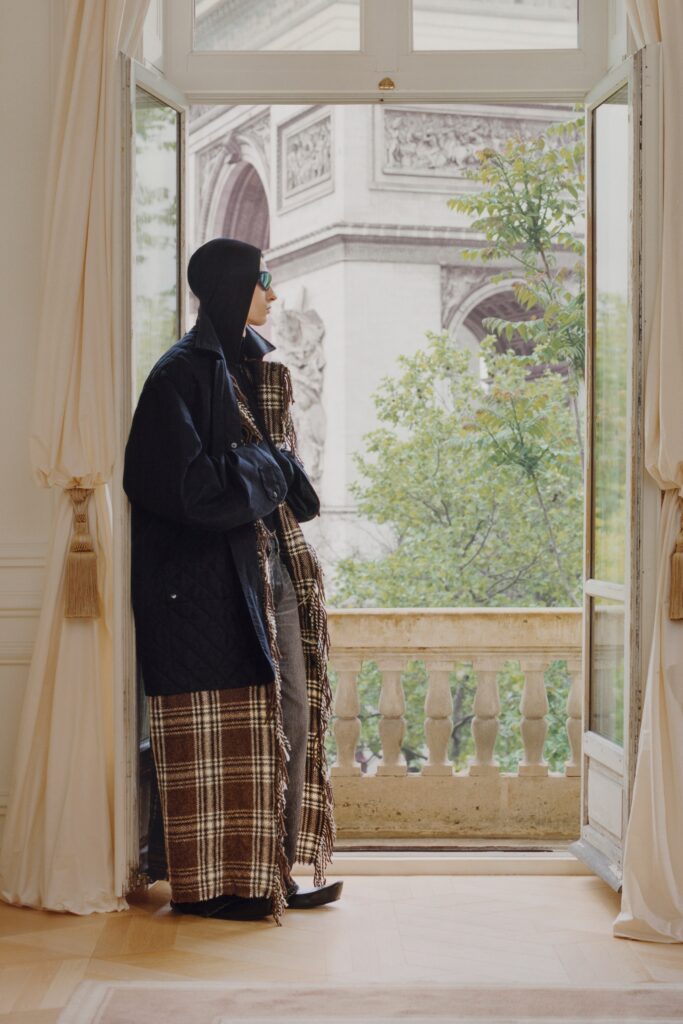 A relaxed black coat layered over a checked dress with long sleeves and a collared design.