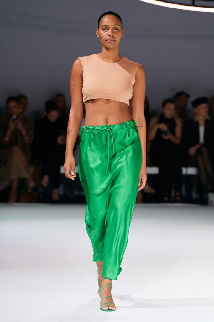 A relaxed beige sleeveless top paired with high-waisted green silk pants featuring an asymmetric design.