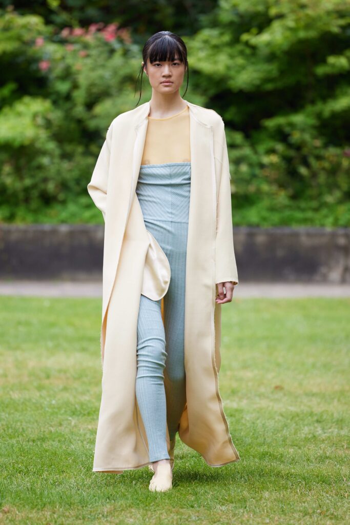A longline beige coat layered over a fitted blue jumpsuit, perfect for a chic runway look.