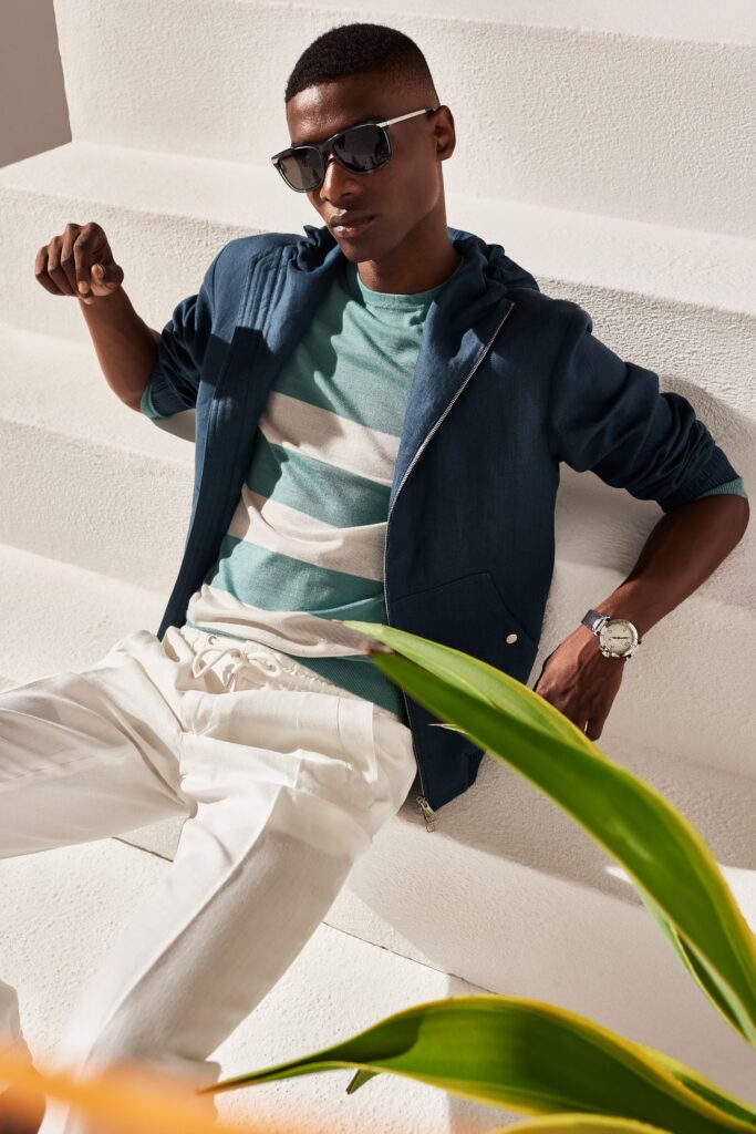 A relaxed blue hooded jacket paired with white pants featuring a striped shirt underneath.