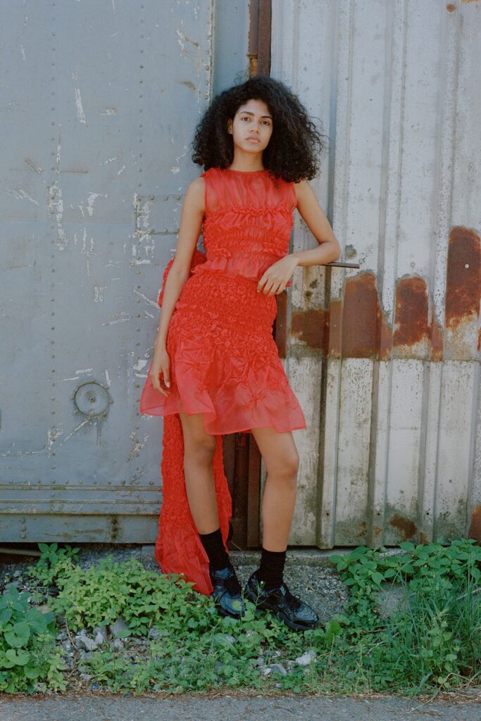 A fitted red silk sleeveless dress with a ruffled design detail.