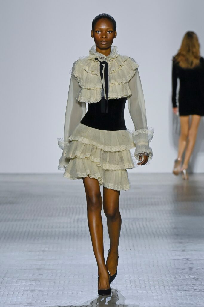 A fitted cream and black dress with long sleeves, a V-neckline, and ruffled tiered design.