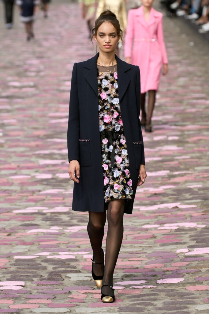 A fitted black floral dress paired with a stylish coat, perfect for a chic runway look.