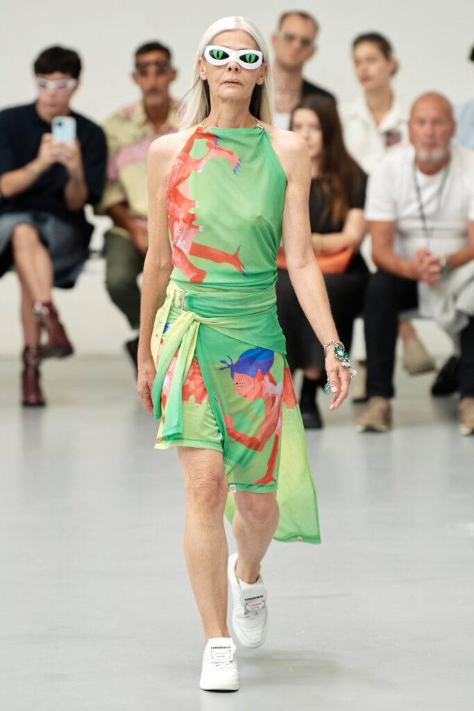A fitted green sleeveless dress with a high neckline and vibrant printed design.