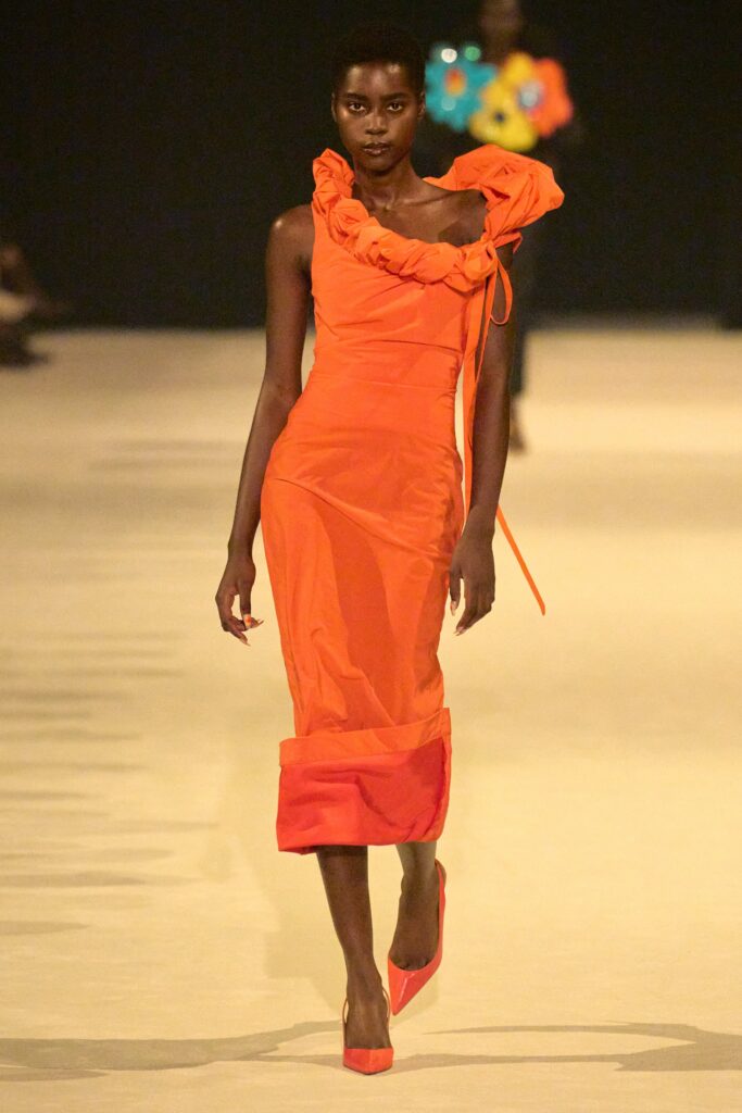 A fitted orange dress with ruffled details and a sleeveless design, perfect for a runway look.