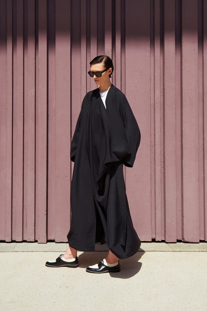 A relaxed black cotton coat with long sleeves and a layered design.