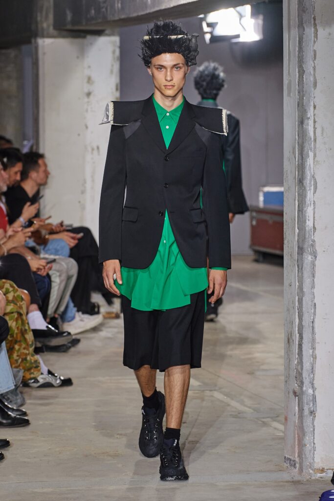 A relaxed black jacket layered over a collared green shirt with an asymmetric design.